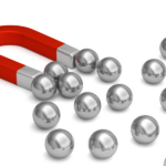 The alt tag for the image can be: Red horseshoe magnet attracting multiple metallic spheres.
