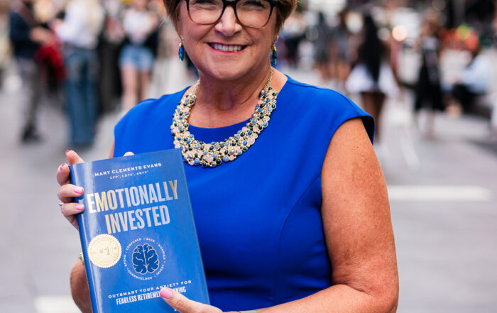 Forbes Books author Mary Clements Evans standing in Times Square with her book “Emotionally Invested,” sharing insights on emotional decision-making and retirement planning on The Covert Code Podcast.