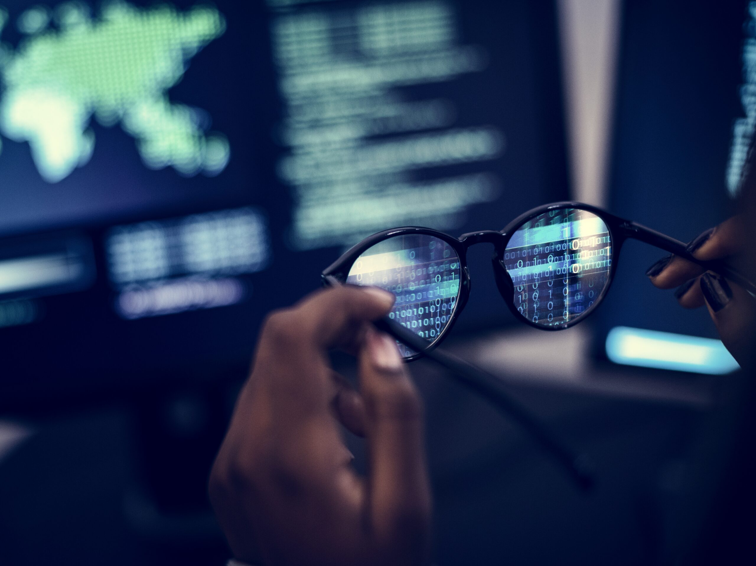 Eyeglasses reflecting binary code in front of computer screens, illustrating data protection in digital advertising and online privacy risks.